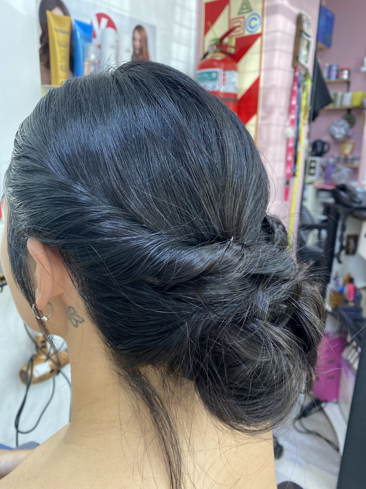 An elegant bridal updo with intricate braiding and delicate floral pearl hair accessories. The lighting is soft and airy, highlighting the texture and professional craftsmanship of the styling. Set in a classic boutique salon environment with warm tones and sophisticated decor.